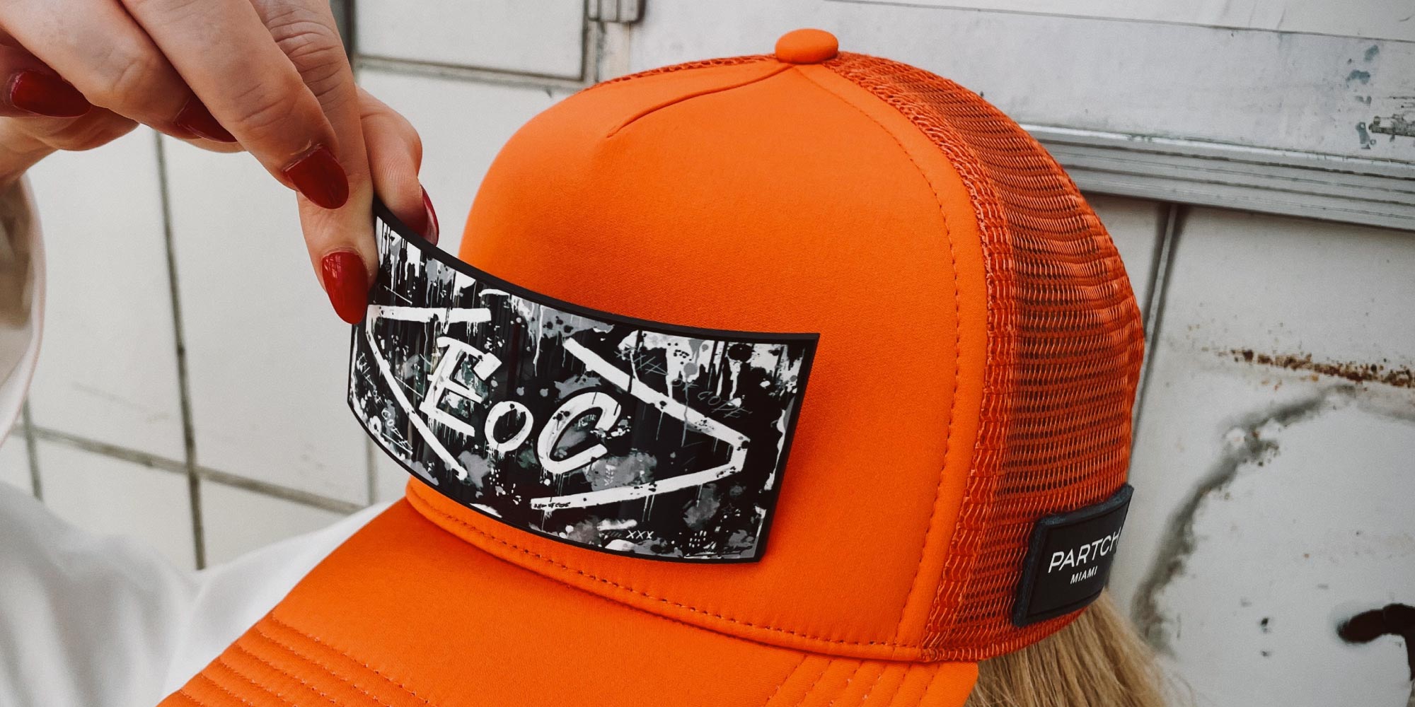 Woman Clipping the Removable Partch Clip ENd of Code on Orange Trucker Hat | PARTCH